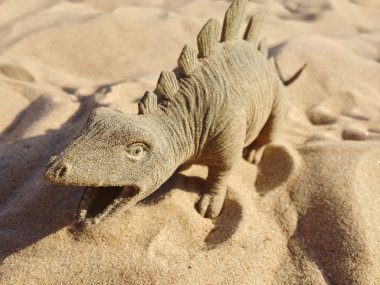 Oyuncak dinozor ayakta kum üzerinde şeklinde.
