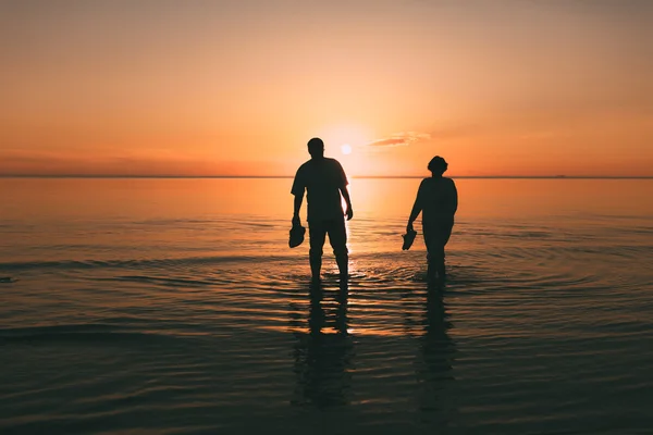 Silueta de pareja adulta que cuesta en el mar y sostiene en calzado de mano . — Foto de Stock