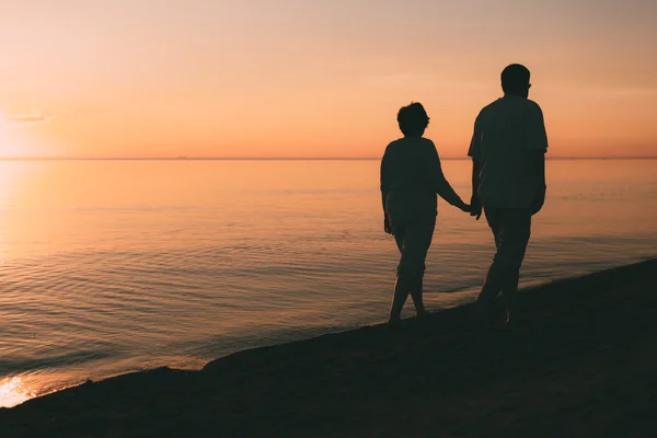 Silueta de pareja adulta camina en la orilla del mar contra una puesta de sol . — Foto de Stock