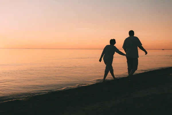 Bir gün batımı karşı sahil siluet yetişkin çift yürür. — Stok fotoğraf
