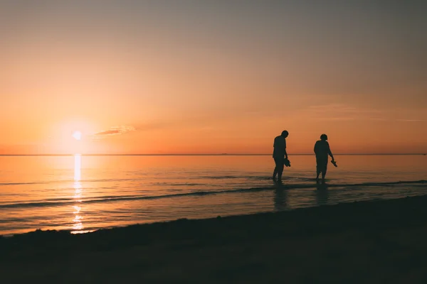 Silhouette eines erwachsenen Paares, das im Meer lebt und Schuhe in der Hand hält. — Stockfoto