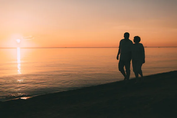 Silhuett av vuxna par promenader på stranden mot en solnedgång. — Stockfoto