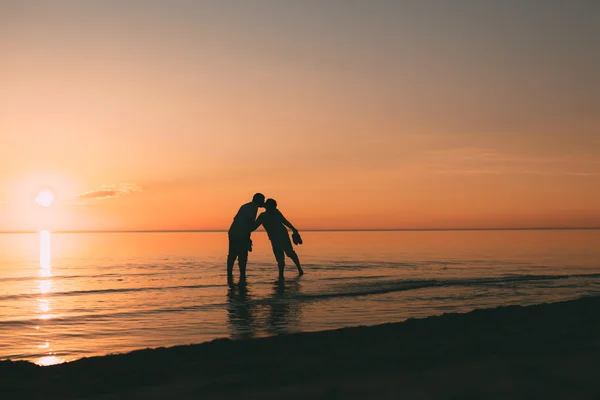 Silhouette eines erwachsenen Paares, das im Wasserkuss vor dem Hintergrund des Sonnenuntergangs steht. — Stockfoto