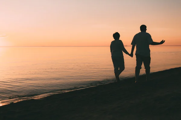 Silhouette eines erwachsenen Paares spaziert am Strand vor Sonnenuntergang. — Stockfoto