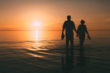Bir gün batımı denizle yetişkin çift ayakta silüeti.