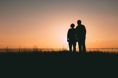 Gün batımında yetişkin çift siluetleri.