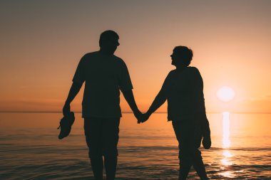 Bir gün batımı denizle yetişkin çift ayakta silüeti.