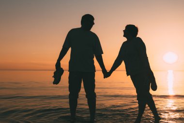 Bir gün batımı denizle yetişkin çift ayakta silüeti.
