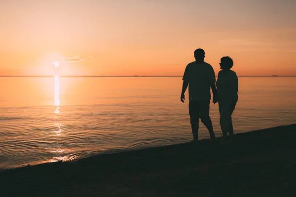 Silhouette of adult couple walks on the seashore against a sunset. — Stock Photo, Image