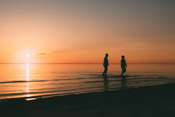 Silhuett av voksne par som står i havet mot en solnedgang. . – stockfoto