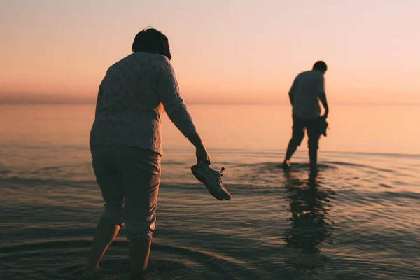 Adult married couple holds shoes in hand and walks on water. — Stock Photo, Image