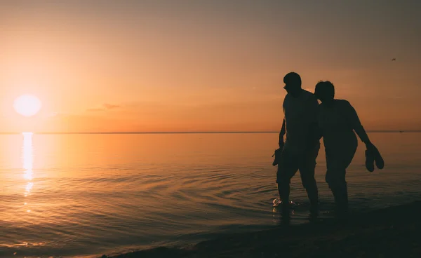 Silhouette eines erwachsenen Paares spaziert am Strand vor Sonnenuntergang. — Stockfoto