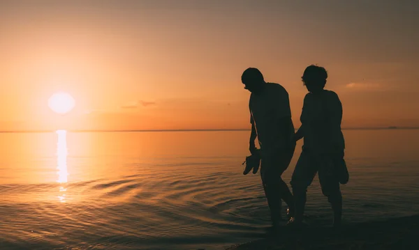 Silueta de pareja adulta camina en la orilla del mar contra una puesta de sol . — Foto de Stock