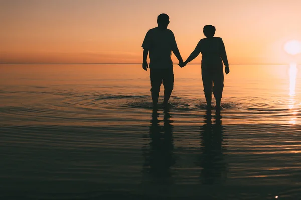 Silueta de pareja adulta de pie en el mar contra una puesta de sol . — Foto de Stock
