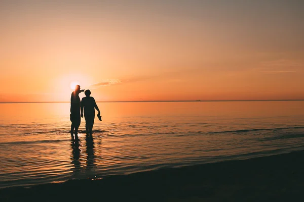 Silhouette of adult couple which costs in the sea and holds in hand footwear. — Stock Photo, Image