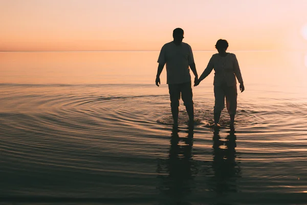 Silueta de pareja adulta de pie en el mar contra una puesta de sol . —  Fotos de Stock