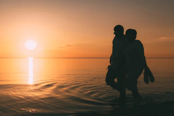 Σιλουέτα του ενήλικα ζευγάρι περπατά στην παραλία ενάντια σε ένα ηλιοβασίλεμα. — Φωτογραφία Αρχείου