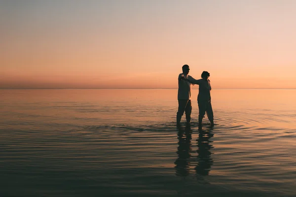 Silueta de pareja adulta de pie en el mar contra una puesta de sol . — Foto de Stock