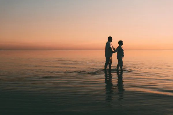 Silhouette eines erwachsenen Paares, das im Meer vor einem Sonnenuntergang steht. — Stockfoto