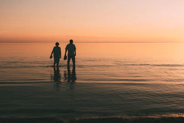 Silhouette eines erwachsenen Paares, das im Meer lebt und Schuhe in der Hand hält. — Stockfoto