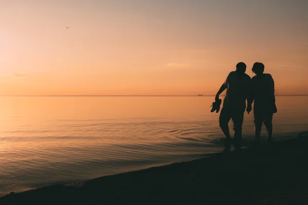 Silhouette di coppie di adulti cammina sulla riva del mare contro un tramonto . — Foto Stock