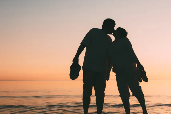 Silhueta de casal adulto em pé no mar contra um pôr do sol . — Fotografia de Stock