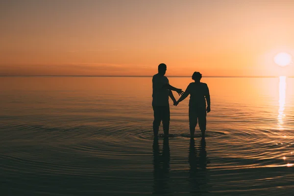Silhouette de couple adulte debout dans la mer contre un coucher de soleil . — Photo