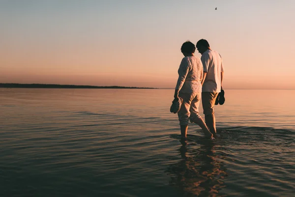 Silueta unui cuplu adult în picioare în mare împotriva unui apus de soare . — Fotografie, imagine de stoc