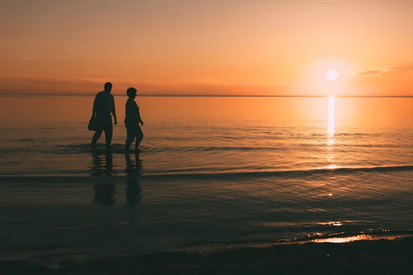 Silhouette of adult couple which costs in the sea and holds in hand footwear. — Stock Photo, Image