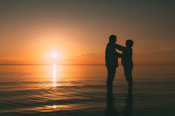 Silhouette di coppia adulta in piedi nel mare contro un tramonto . — Foto Stock