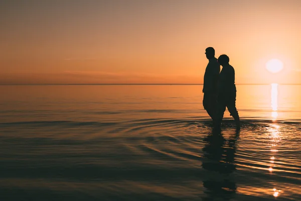 Silhouette eines erwachsenen Paares, das im Meer vor einem Sonnenuntergang steht. — Stockfoto