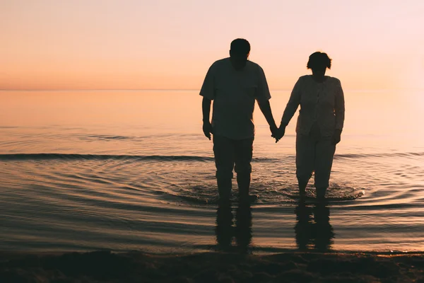 Silueta de pareja adulta de pie en el mar contra una puesta de sol . — Foto de Stock