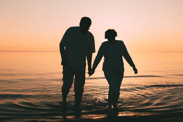 Silueta de pareja adulta de pie en el mar contra una puesta de sol . — Foto de Stock