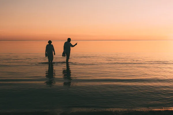 Silhouette eines erwachsenen Paares, das im Meer lebt und Schuhe in der Hand hält. — Stockfoto