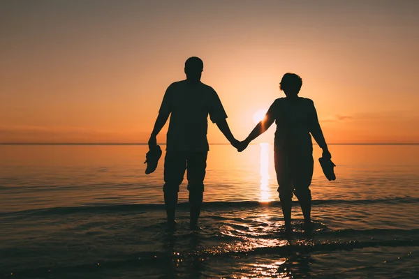 Silueta de pareja adulta de pie en el mar contra una puesta de sol . — Foto de Stock