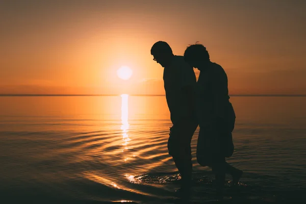 アダルト カップルのシルエットに対して夕日の海岸の上を歩く. — ストック写真