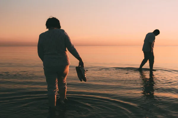 Erwachsenes Ehepaar hält Schuhe in der Hand und geht auf dem Wasser. — Stockfoto