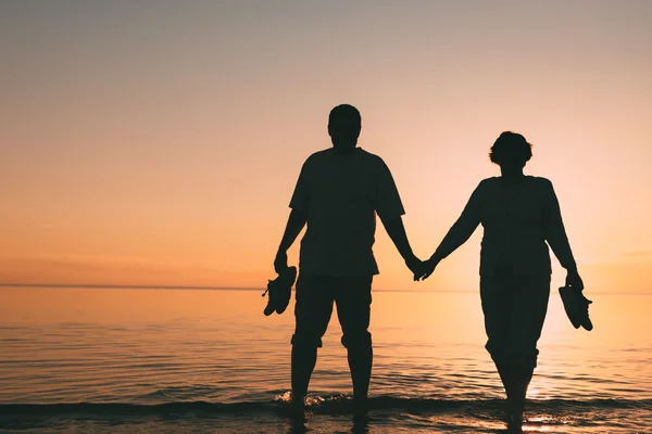 Silhouette eines erwachsenen Paares, das im Meer vor einem Sonnenuntergang steht. — Stockfoto