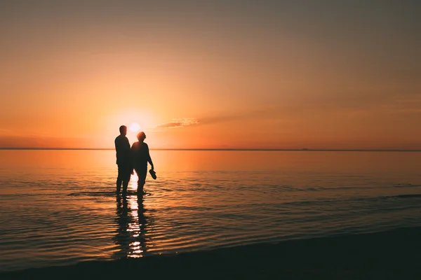 Silhouette eines erwachsenen Paares, das im Meer lebt und Schuhe in der Hand hält. — Stockfoto