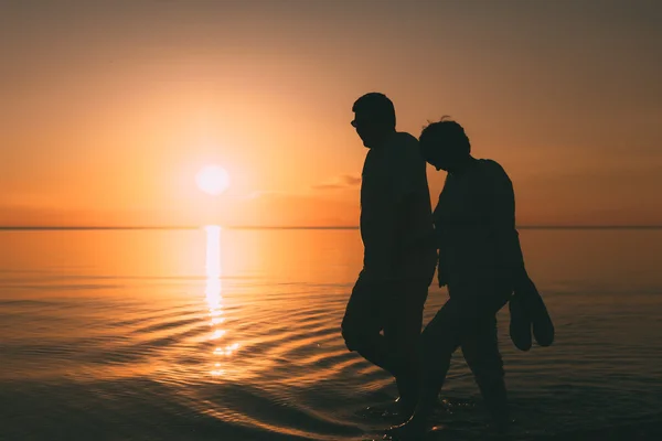 Силует дорослої пари гуляє на березі моря на захід сонця . — стокове фото