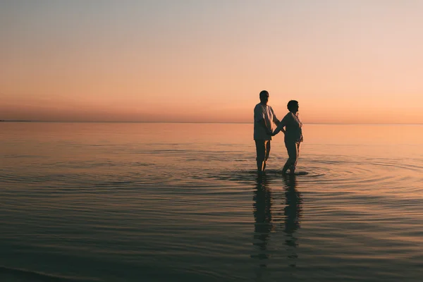 Silhuett av voksne par som står i havet mot en solnedgang. . – stockfoto