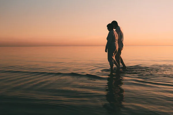 Silhouette eines erwachsenen Paares, das im Meer vor einem Sonnenuntergang steht. — Stockfoto