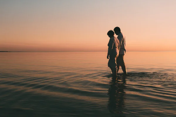 Silhouette eines erwachsenen Paares, das im Meer vor einem Sonnenuntergang steht. — Stockfoto