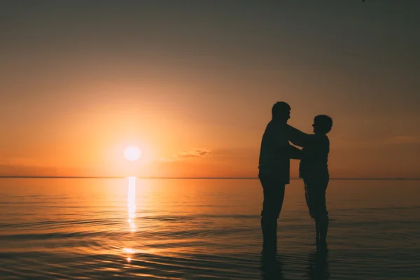 Silhouette eines erwachsenen Paares, das im Meer vor einem Sonnenuntergang steht. — Stockfoto