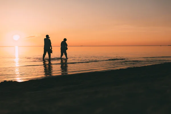 Silueta de pareja adulta que cuesta en el mar y sostiene en calzado de mano . — Foto de Stock