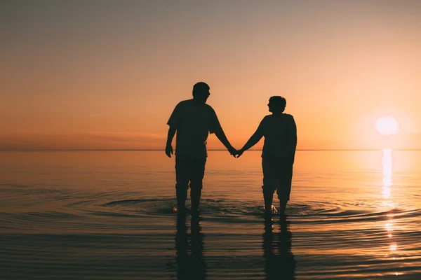 Silhouette eines erwachsenen Paares, das im Meer vor einem Sonnenuntergang steht. — Stockfoto