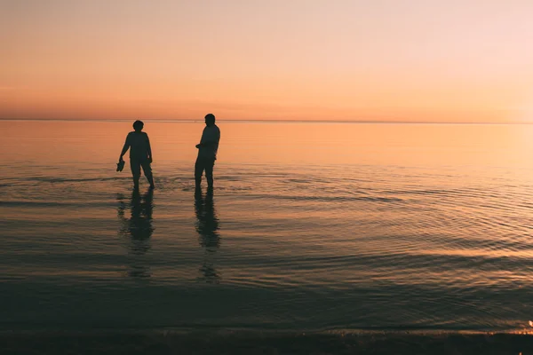 Silhouette eines erwachsenen Paares, das im Meer lebt und Schuhe in der Hand hält. — Stockfoto