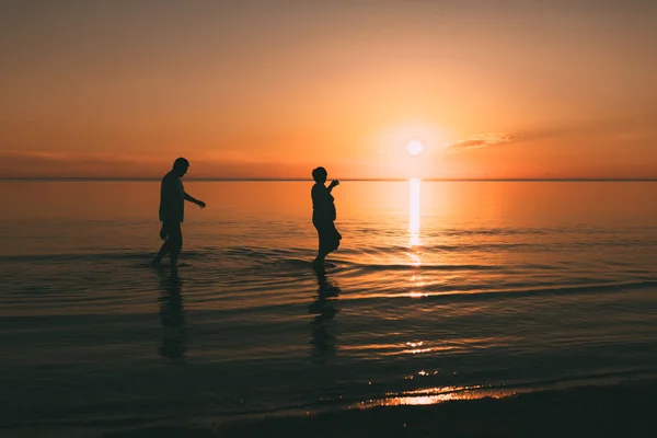 Silhouette eines erwachsenen Paares, das im Meer lebt und Schuhe in der Hand hält. — Stockfoto