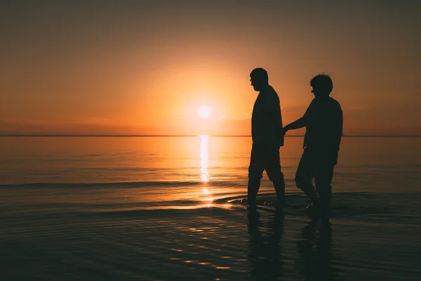 Silhuet af voksne par stående i havet mod en solnedgang . - Stock-foto