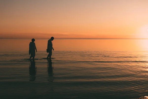 Silhouette eines erwachsenen Paares, das im Meer lebt und Schuhe in der Hand hält. — Stockfoto